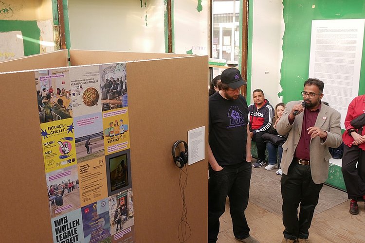 Aju John im Pavillion Klassenzimmer der Zukunft vor der ASH Berlin. Er hält ein Mikrofon in der Hand und spricht zu den Gästen die im Pavillion stehen. 