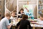 Eine Gruppe Studierende sitzt am großen Arbeitstisch der Werkstatt und malt an Bildern.