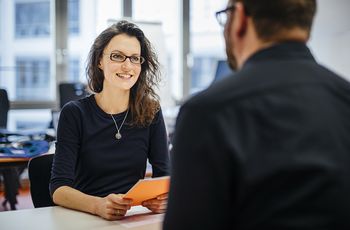 Beratungsgespräch: die Forschungsreferentin sitzt einem Wissenschaftler an einem Tisch gegenüber und berät ihn.