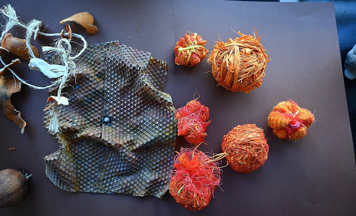 Zu sehen sind verschiedene zusammengebundene rot-orangene Kugeln, die neben einer texturierten braunen Fläche liegen.