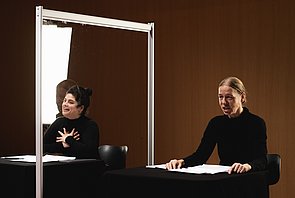 Die zwei Sprecherinnen am Tisch, zwischen ihnen eine durchsichtige Stellwand