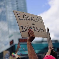 Eine Hand hält ein Schild hoch. Darauf steht: Equality in Diversity.