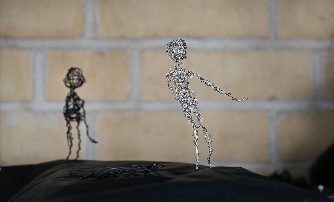 Zu sehen ist sind zwei hintereinander, auf einem schwarzen Tuch stehende, Wesen aus schwarzem bzw. silbernen Draht