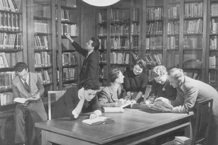 Historische schwarz-weiß-Aufnahme von Wissenschaftlerinnen und Wissenschaftlern, die sich in einer mit vielen Büchern gefüllten Bibliothek befinden und miteinander diskutieren.
