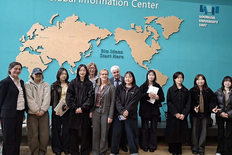 Die Delegation der ASH Berlin und Studierende der Soongsil University vor einem Wandbild mit einer Weltkarte. Über der Weltkarte steht der Schriftzug: Global Information Center