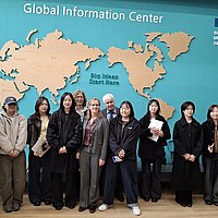 Die Delegation der ASH Berlin und Studierende der Soongsil University vor einem Wandbild mit einer Weltkarte. Über der Weltkarte steht der Schriftzug: Global Information Center