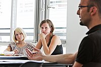 Unterrichtssituation: Dozent sitzt vor 2 Studierenden und erklärt etwas.