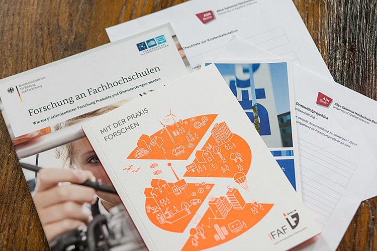 Blick von oben auf verschiedene Broschüren von Drittmittelgebern, darunter das IFAF Berlin, lesbar sind die Titel "Forschung an Fachhochschulen" und "Mit der Praxis forschen"