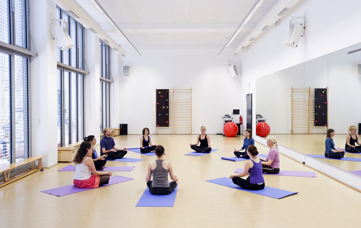Menschen sitzen auf Sportmatten im Kreis und machen Yogaübungen