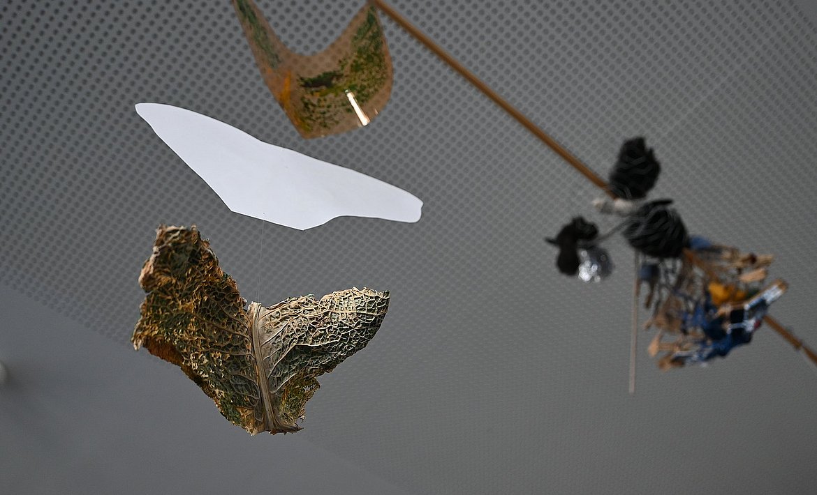 Zu sehen ist ein an einem Faden hängendes Werk aus Kohl, Folie und Papier.