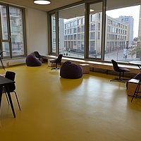 Eine Selbstlernfläche im Neubau, ausgestattet mit verschiedenen Sitzgelegenheiten. Durch große Fenster ist der Koschkaplatz und das Hauptgebäude der ASH Berlin zu sehen