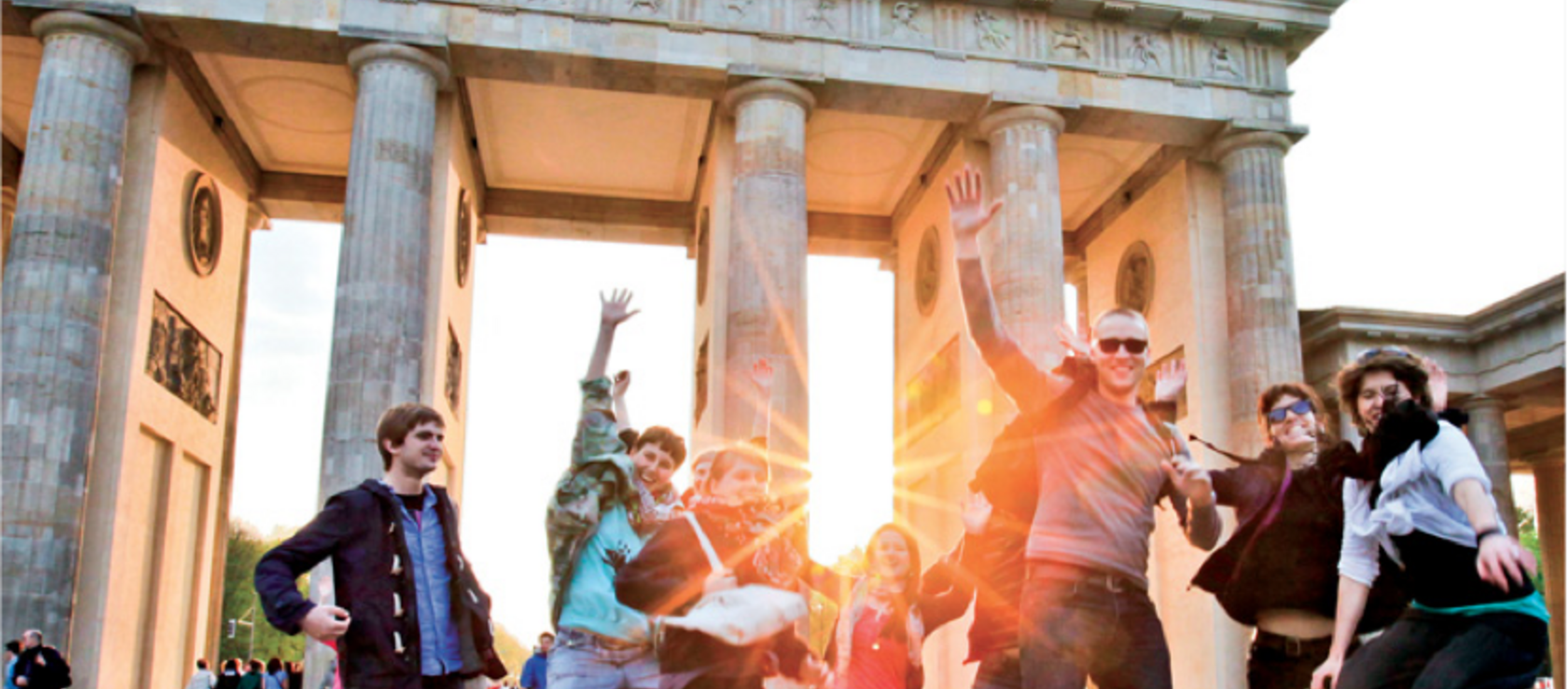 Vor dem Berliner Panorama des Brandenburger Tors springt eine Gruppe Studierender in die Luft.
