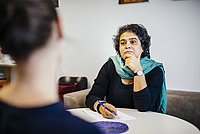 Interview-Situation: Eine Probantin ist nur von hinten sichtbar und scheint zu erzählen, eine Professorin hört aufmerksam zu.